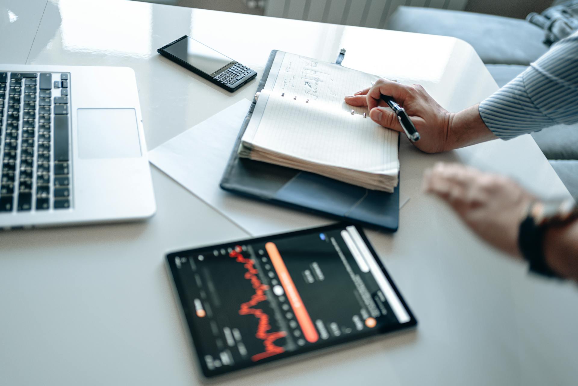 A person analyzing business data using a tablet, laptop, and notebook for efficient work.