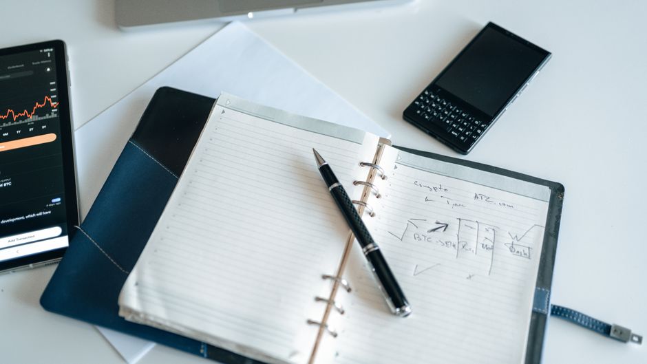 Flat lay of a workspace with a notebook, pen, and electronic devices, ideal for productivity.
