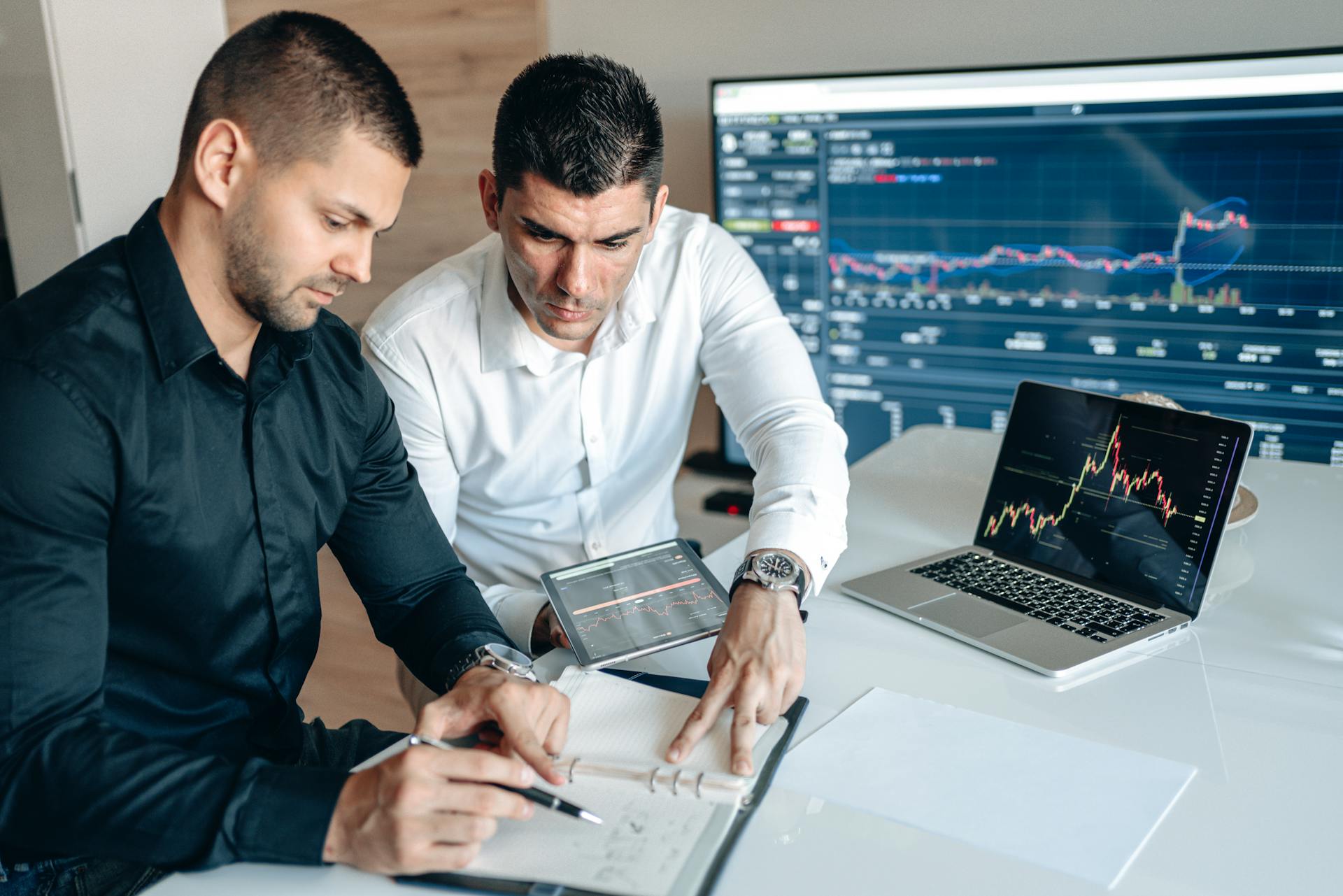 Two professionals analyzing financial charts in an office setting with laptops and screens.