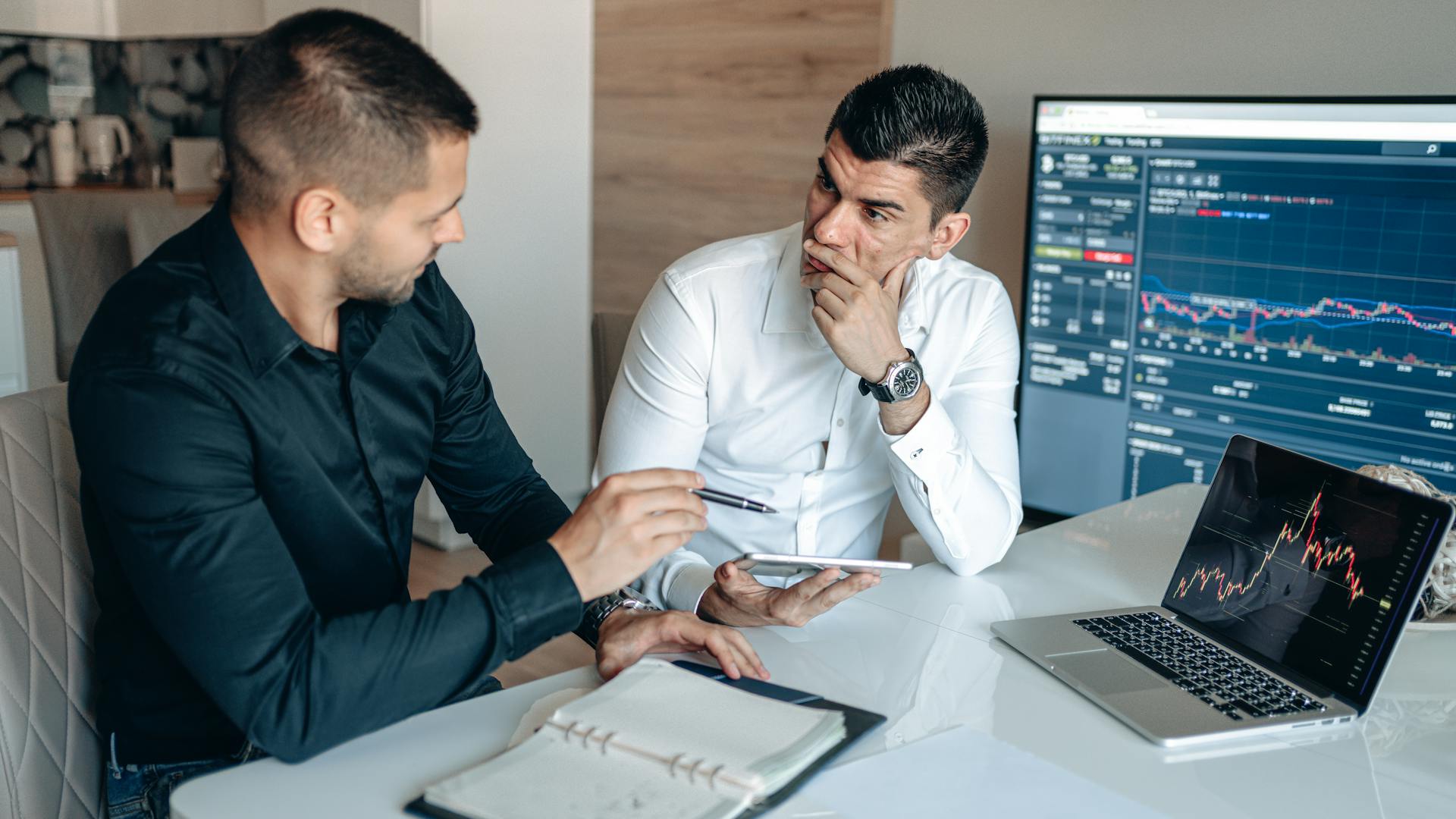 Traders Having a Conversation while Sitting on a Chair in Front of Monitors with Crypto Graph