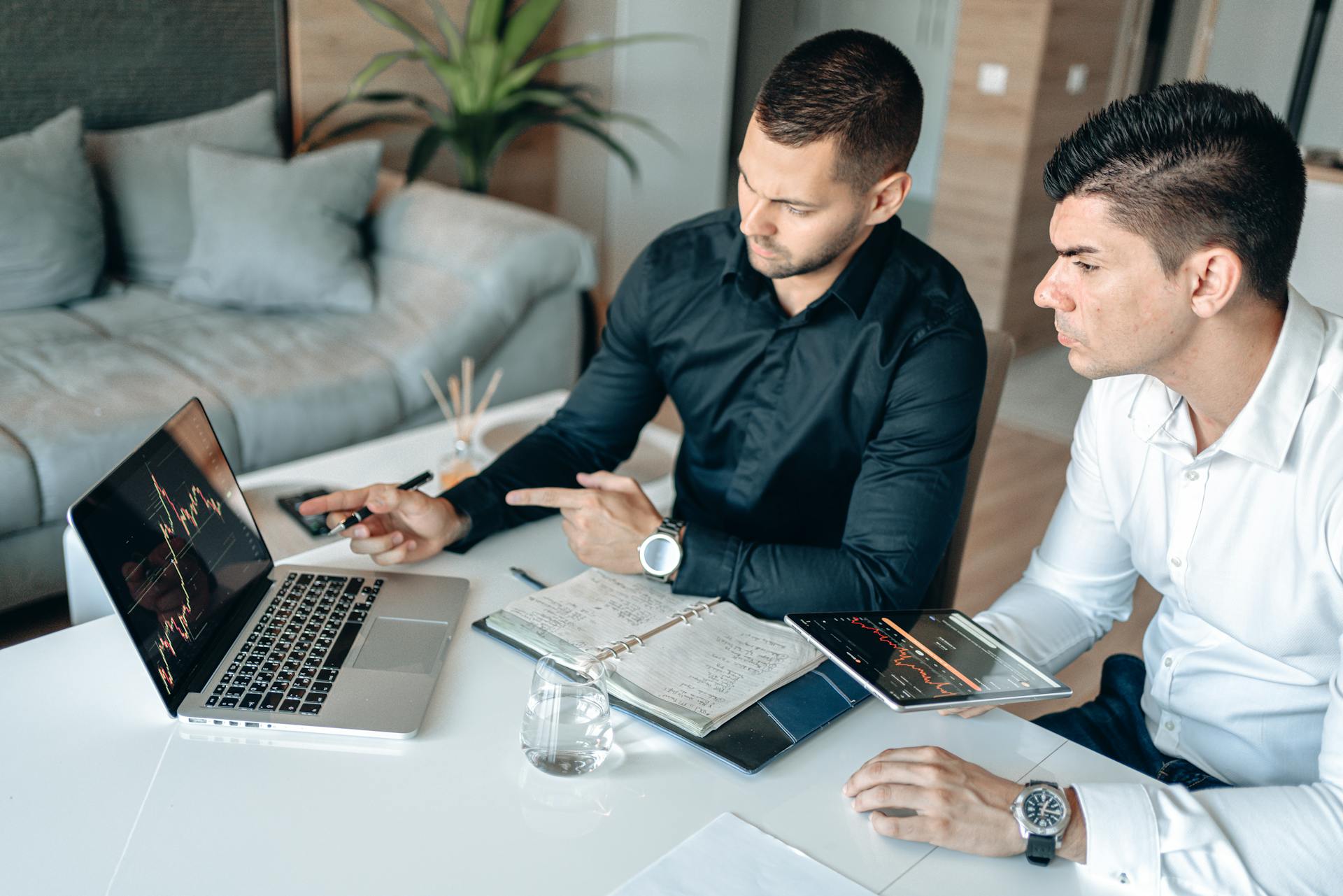 Two men in a business meeting analyzing digital charts on laptop and tablet.