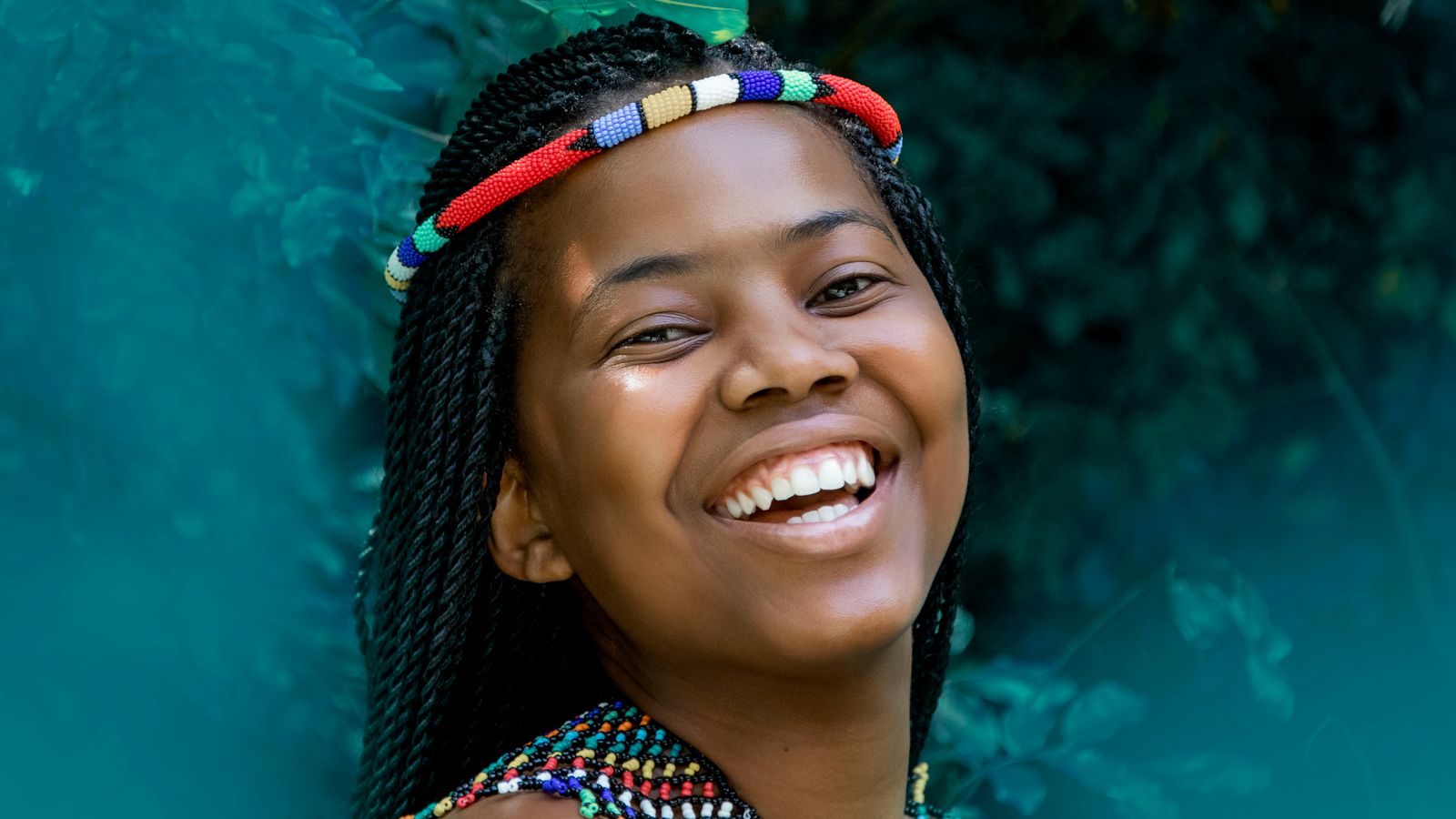 A woman wearing colorful beaded headband and necklace smiling to the camera, South Africa