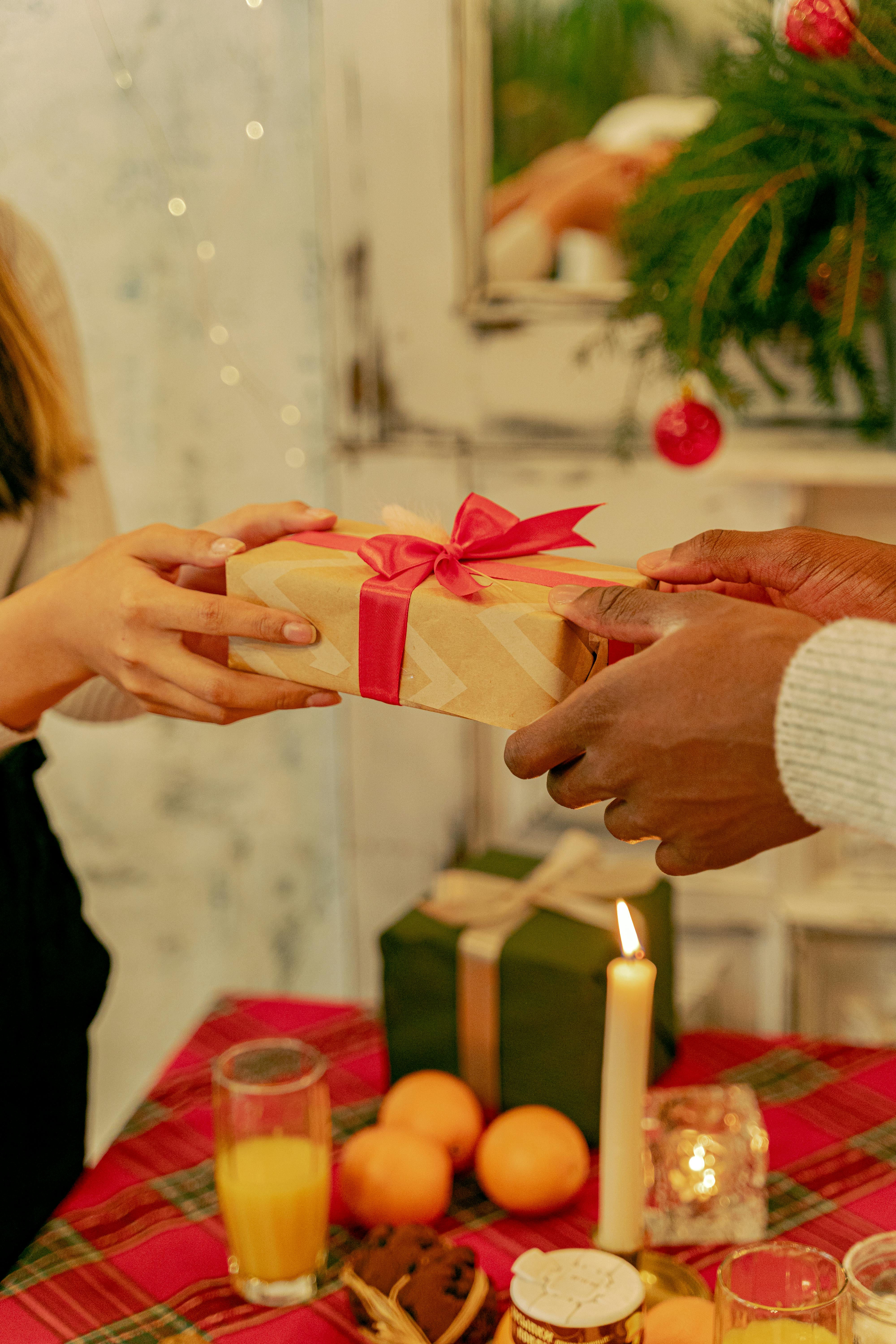 Two people exchange gifts in a cozy Christmas setting with candles and holiday decor.