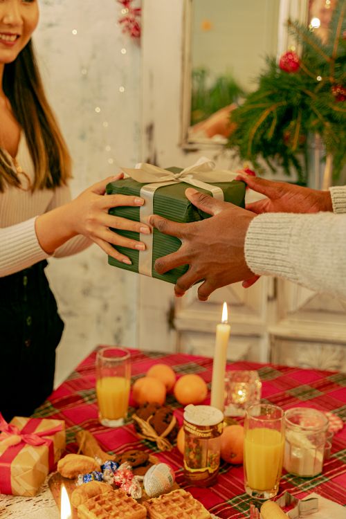 Free A warm holiday scene with people exchanging gifts at a festive decorated table. Stock Photo