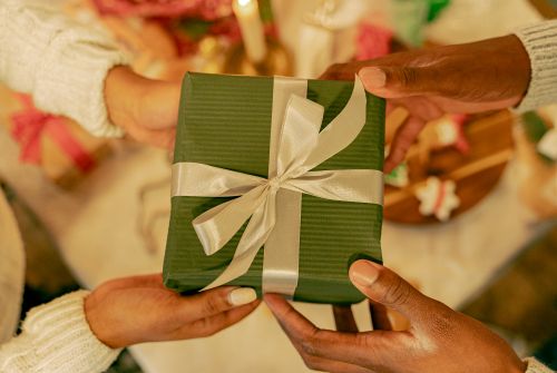 Free A close-up of hands exchanging a green gift, symbolizing celebration and giving. Stock Photo