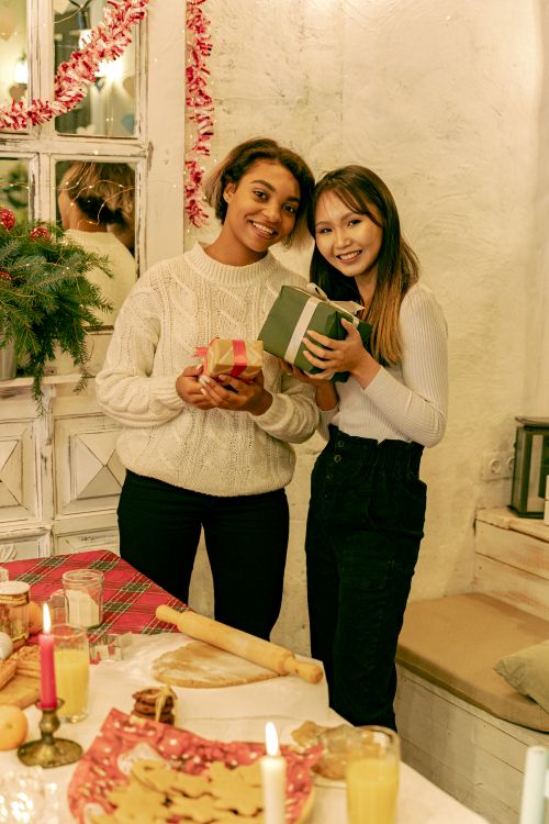 Free Two women exchanging gifts in a festive indoor setting with candles and decorations. Stock Photo