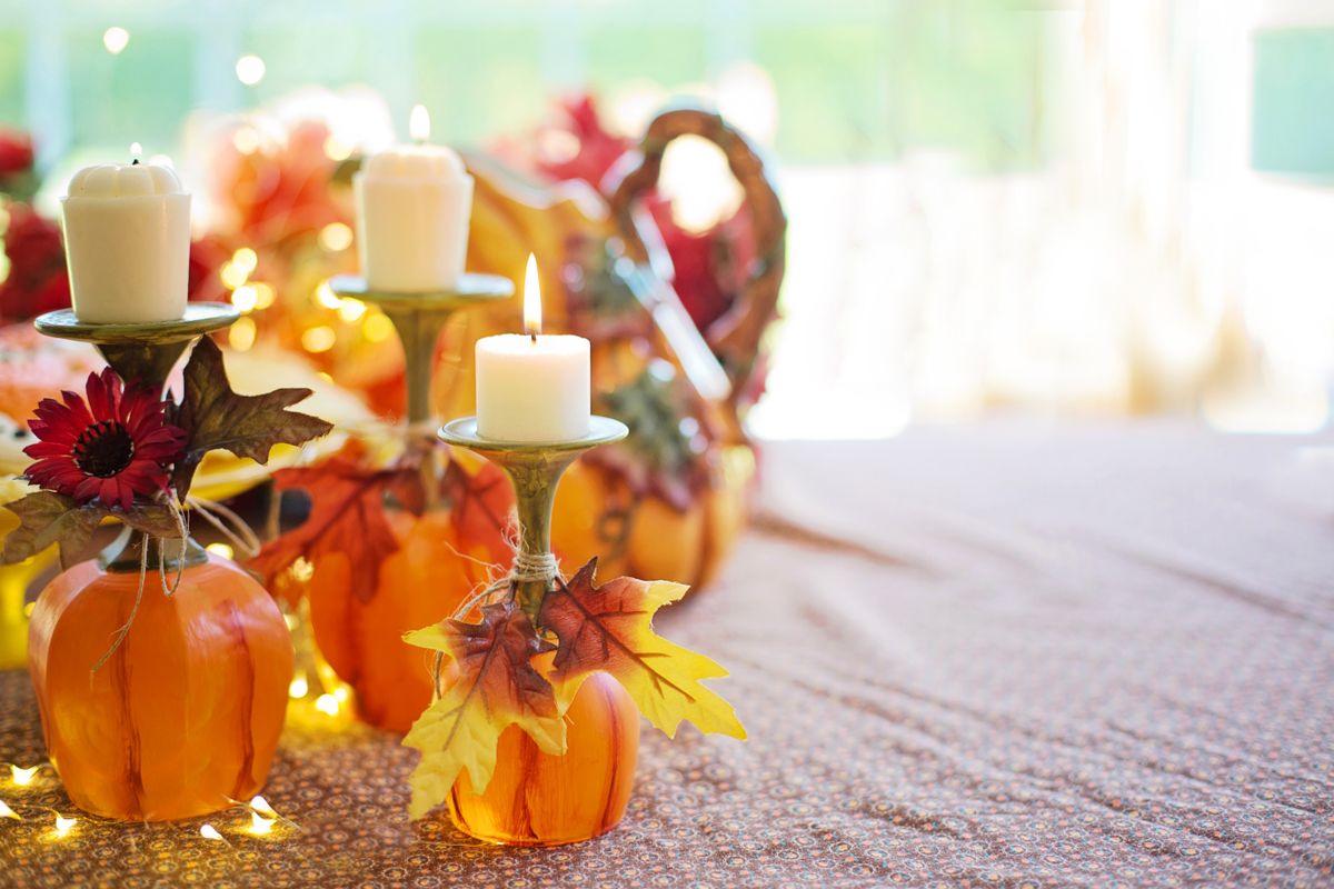 Warm autumn table decor featuring pumpkins, candle holders, and fall leaves. Stock Photo.