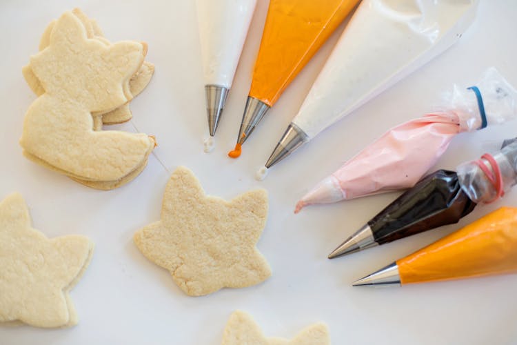 Piping Bags With Icing Beside Cookies On A White Surface