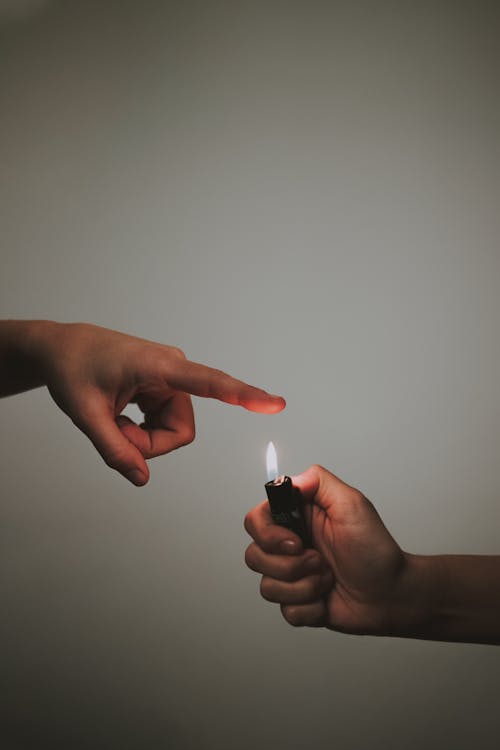 Crop anonymous person demonstrating warm flame from cigarette lighter against gray background in studio
