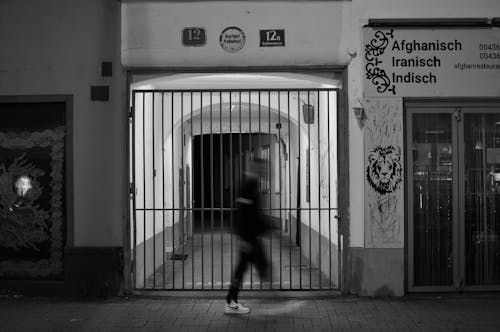 Grayscale Photo of a Person Walking Pass the Steel Gate