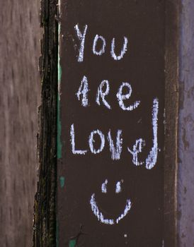 Shabby wooden board saying you are loved with positive smile written with chalk