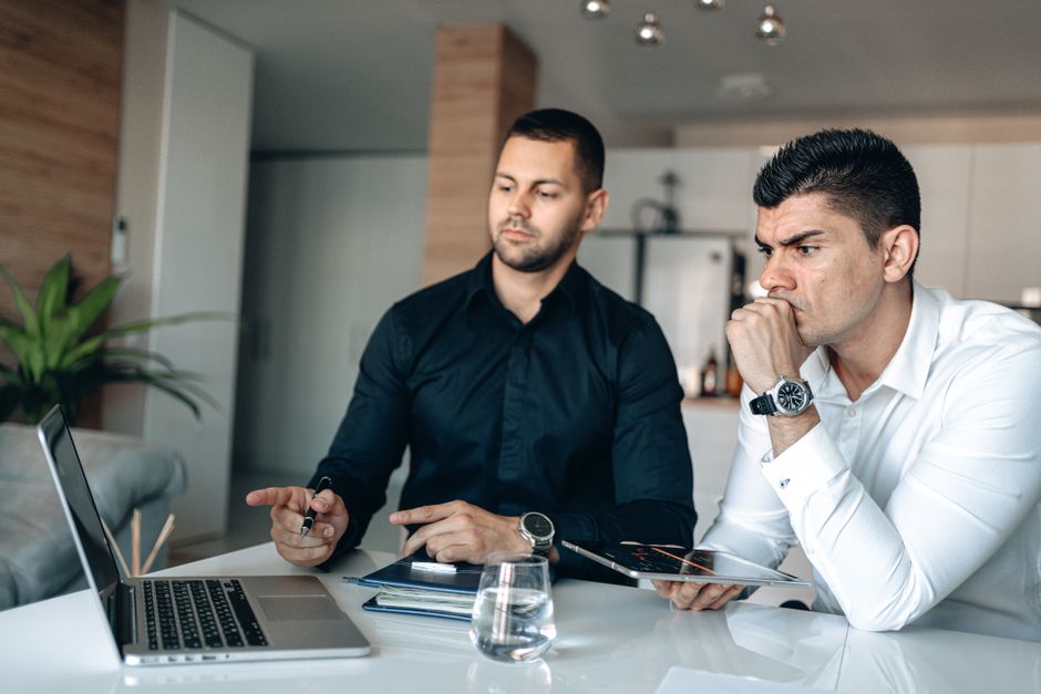 Two men in office attire focused on laptop, discussing business strategies. Two men in office attire focused on laptop, discussing business strategies.