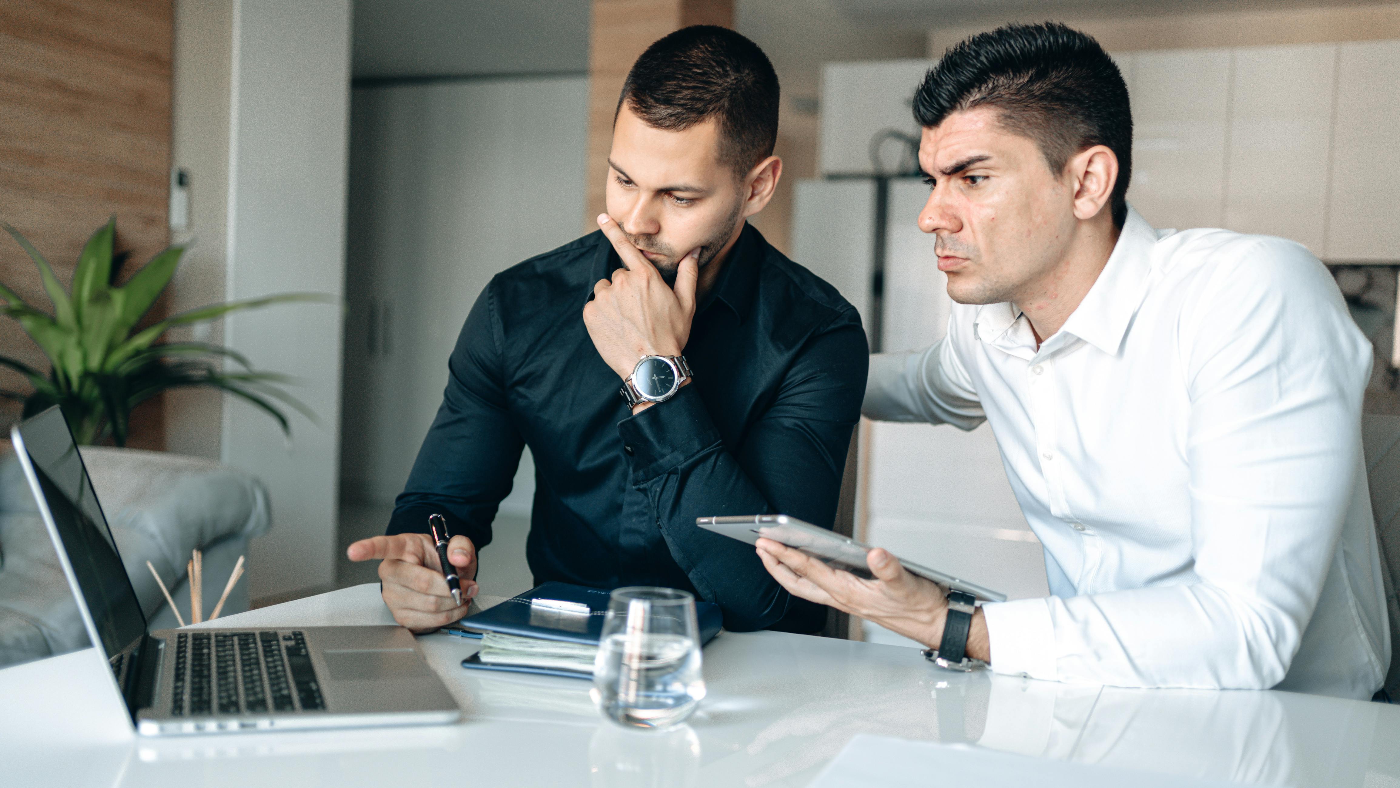 two men sitting looking at a laptop on a white table