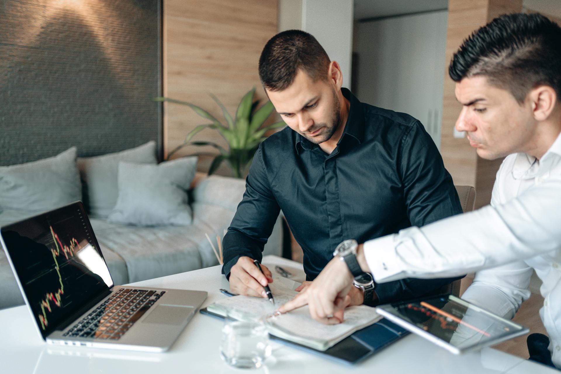 Two businessmen analyzing financial data on a laptop during a meeting.