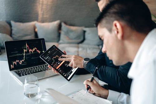 Free Two businessmen analyzing stock charts on a laptop and tablet in an office setting. Stock Photo