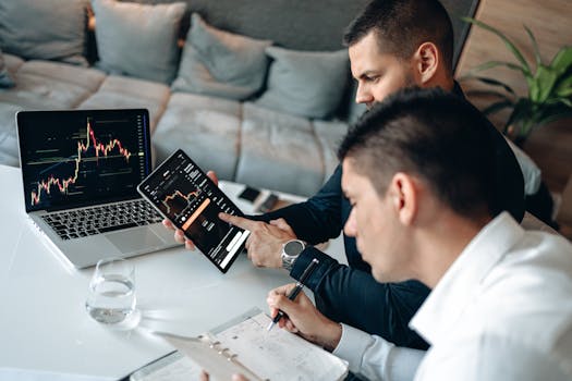 Two businessmen discussing financial charts on devices at a modern indoor setting.