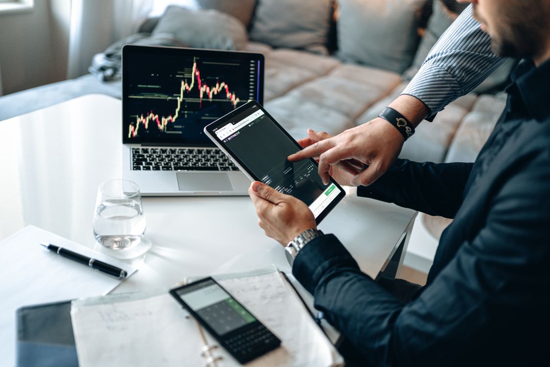 Free Professionals reviewing stock market trends on a tablet and laptop, discussing investment strategies. Stock Photo