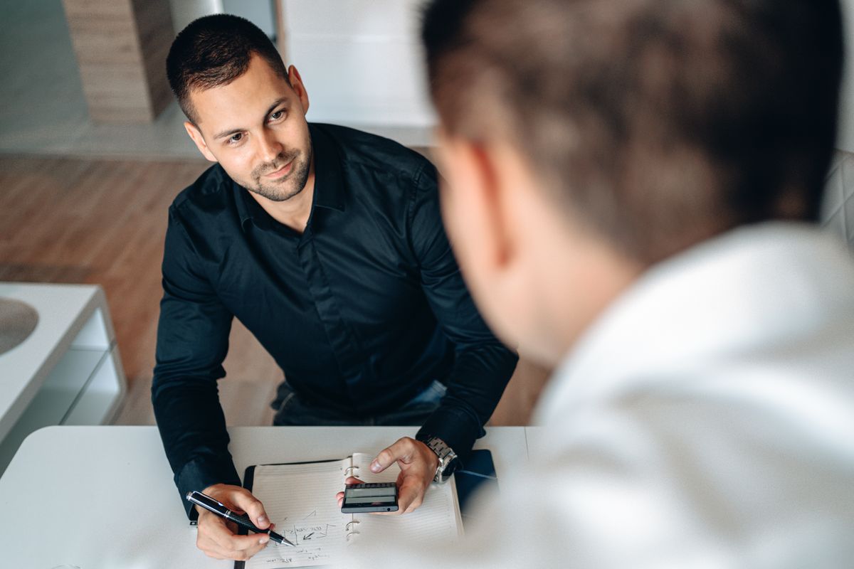 Two men in a business meeting indoors, discussing and taking notes
