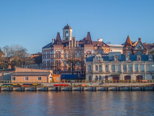Free Beautiful historic building with intricate architecture by a serene riverside under a clear blue sky. Stock Photo