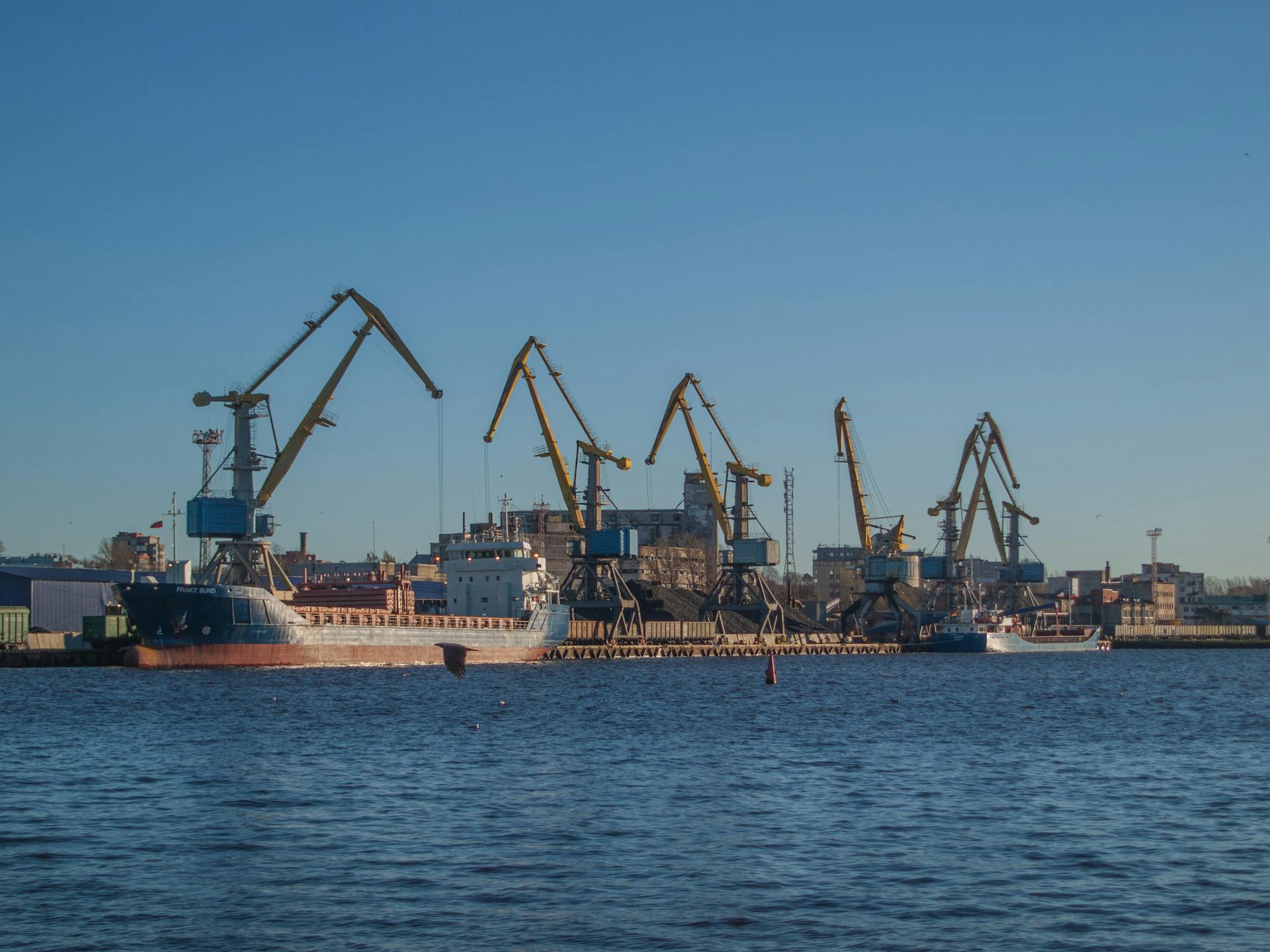 Image of an industrial shipyard with cranes and ships on a sunny day.