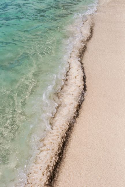 From above of clear turquoise ocean with foamy waves rolling on smooth sandy beach on sunny day