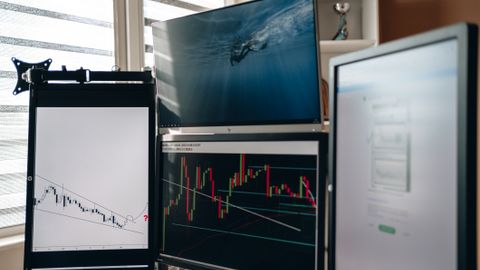 A home office setup featuring multiple monitors displaying trading charts and data analysis.