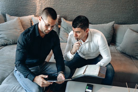 Two professionals engage in a strategic discussion using a digital tablet and notebook indoors.