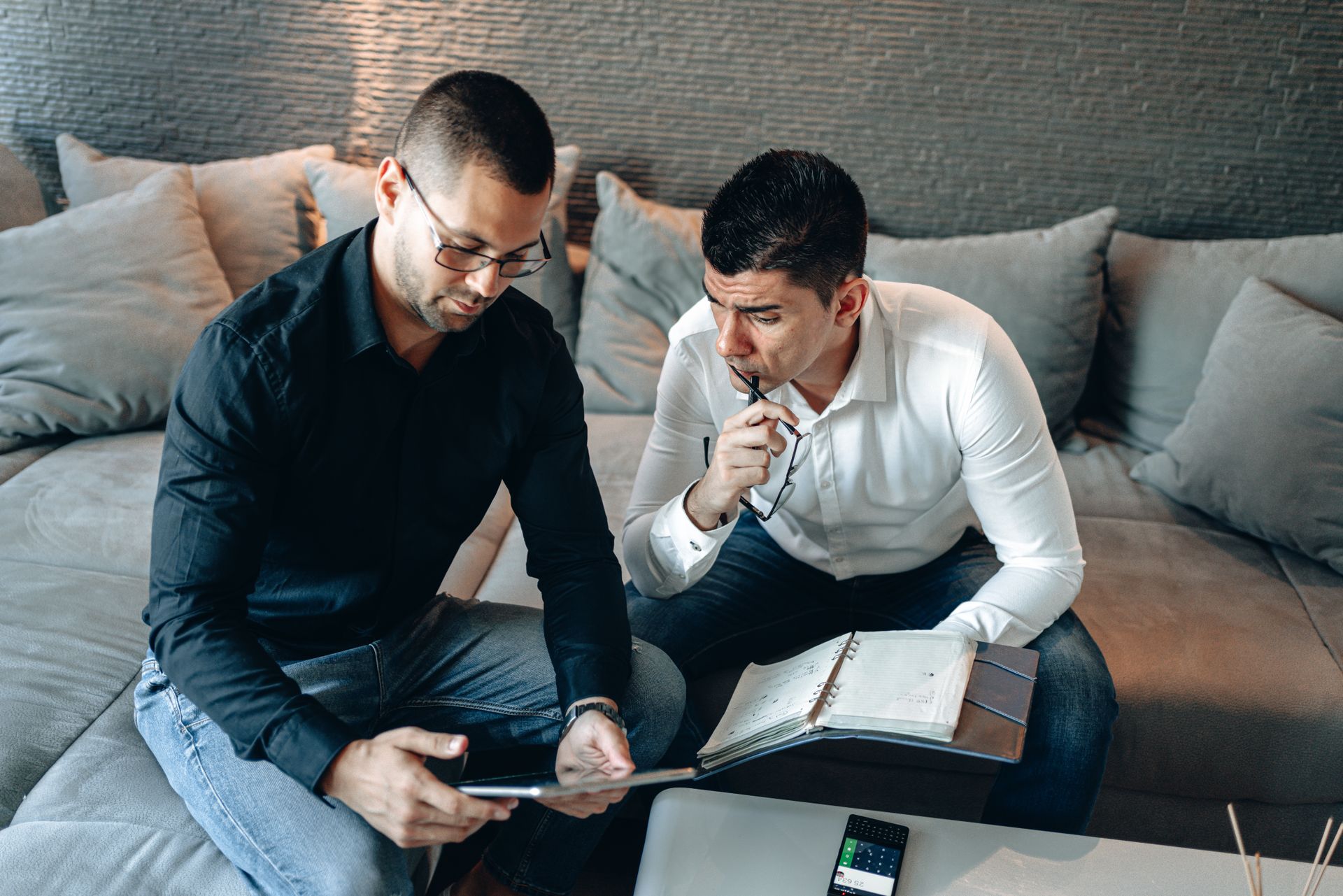 Two professionals engage in a strategic discussion using a digital tablet and notebook indoors.