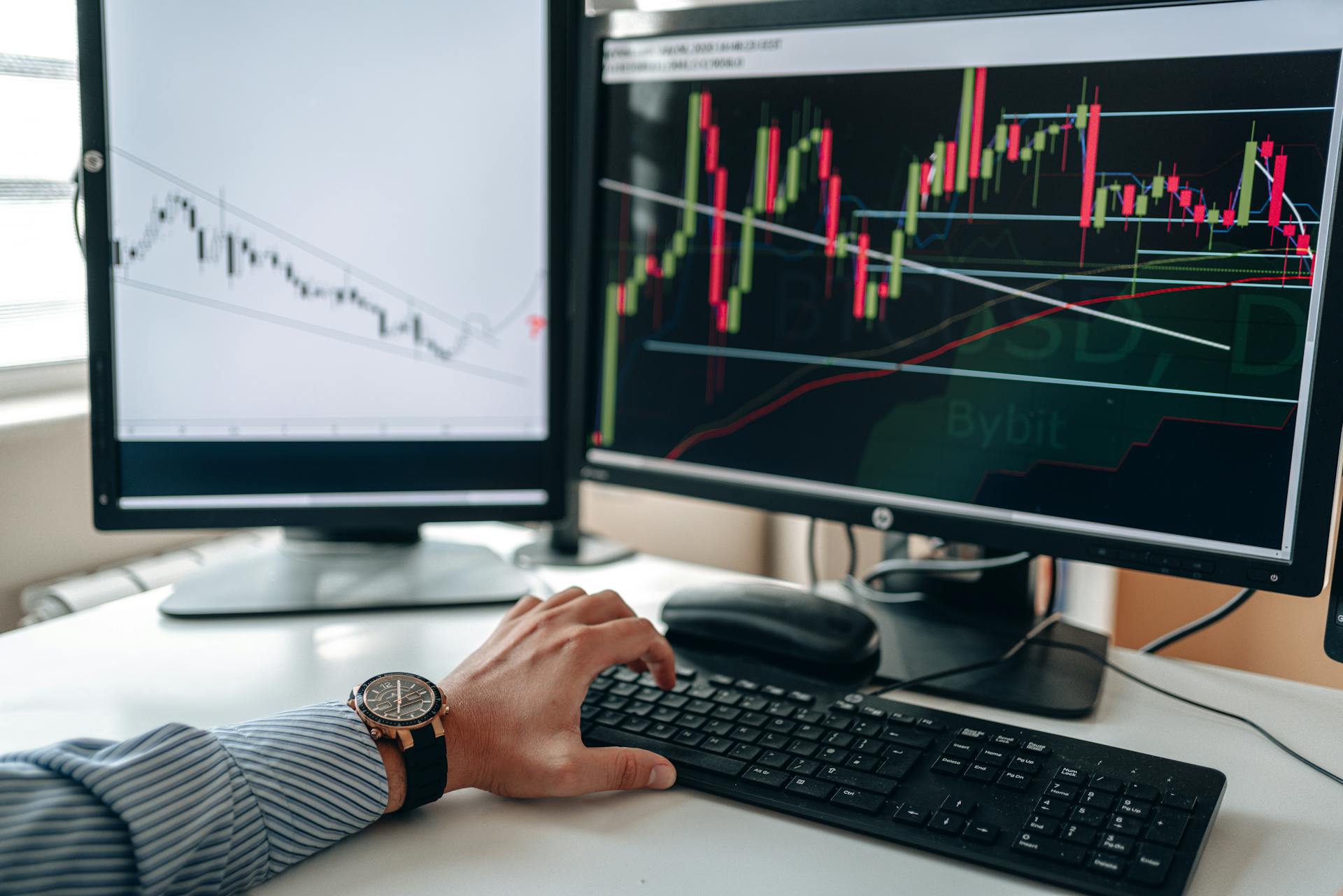 A businessperson using dual monitors to analyze stock market trends with charts and graphs.