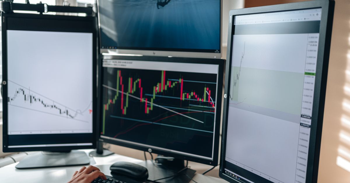 Multi-monitor trading workstation with financial charts and market data, representing CFD trading strategy analysis