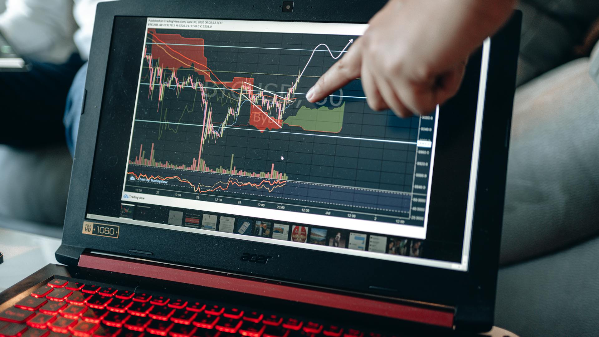 A person points at graph on laptop, analyzing stock trends for investment insights.