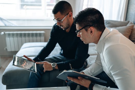 Two men in business attire analyzing financial data on tablet in office.