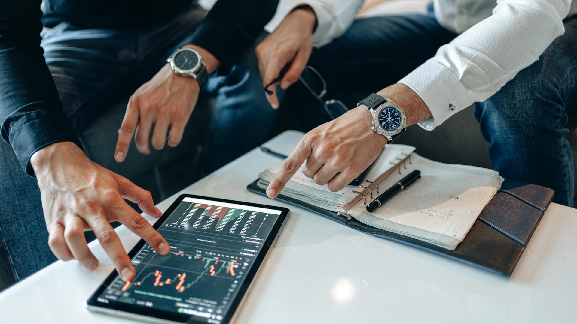 Two businessmen discussing financial data on a tablet during a meeting.