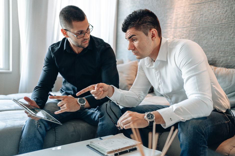 Two men in a home office discuss work on a tablet, highlighting teamwork and collaboration. Two men in a home office discuss work on a tablet, highlighting teamwork and collaboration.
