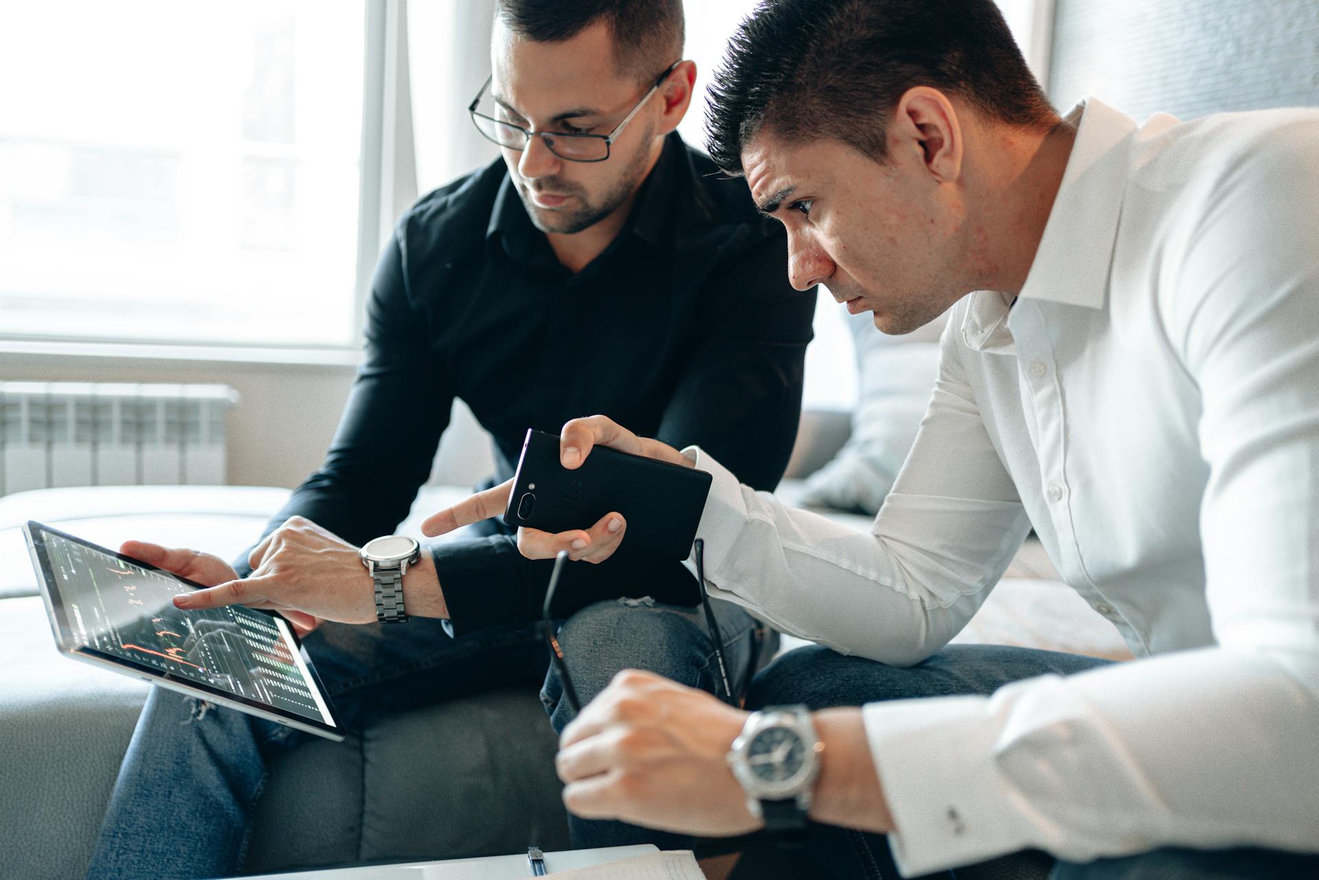 Two men analyzing financial data on a digital tablet indoors in a professional setting.