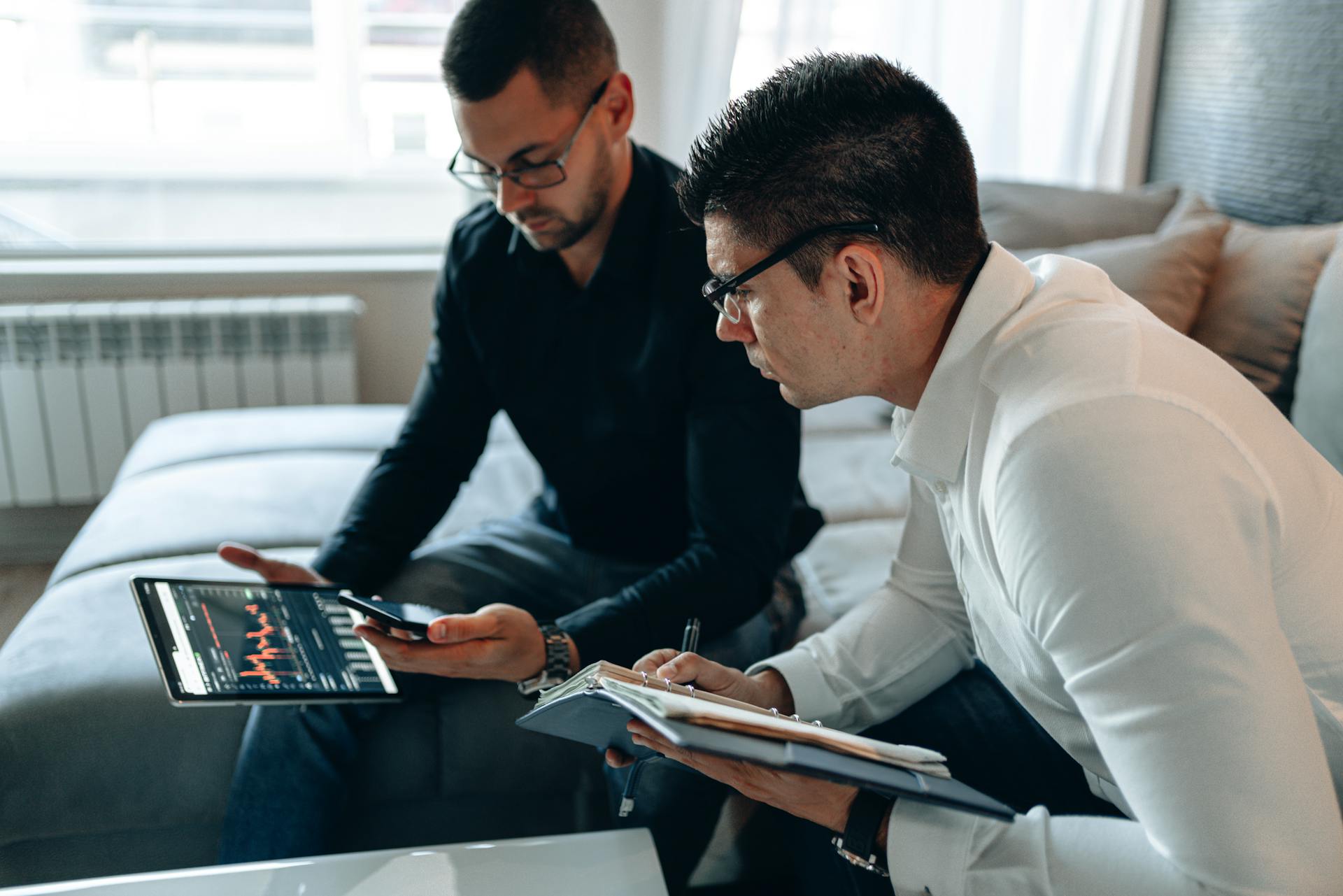 Two businessmen analyzing financial data on a tablet in a modern office setting.