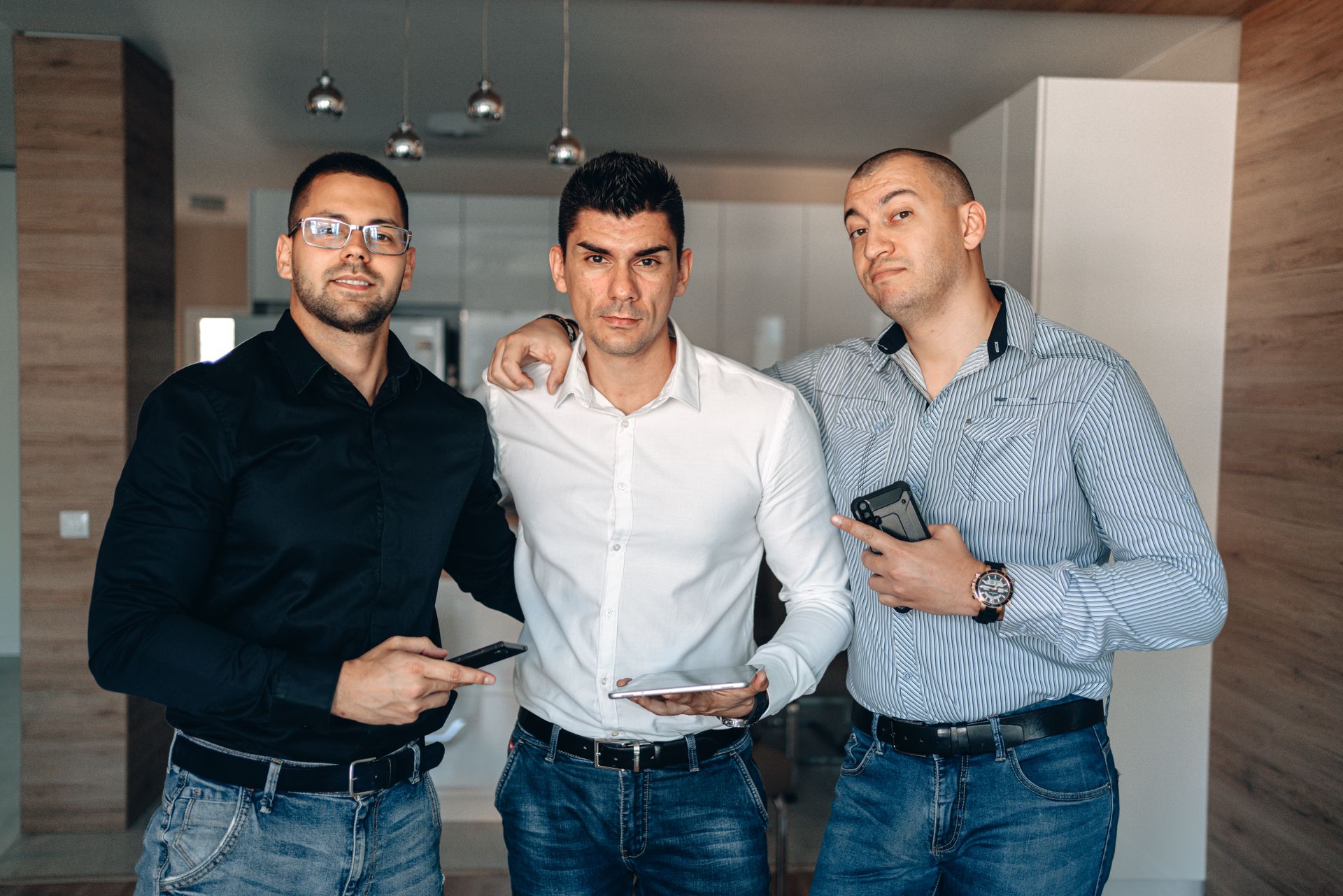 Group of three adult men with digital devices posing in a modern indoor setting.