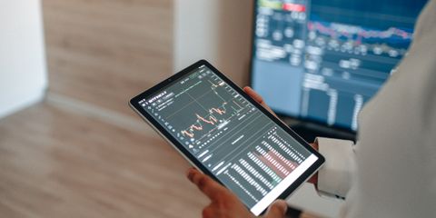 A person uses a tablet to monitor stock market trends and real-time trading graphs.
