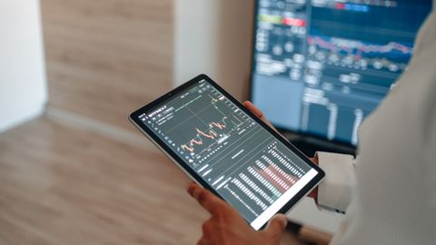 A person uses a tablet to monitor stock market trends and real-time trading graphs.