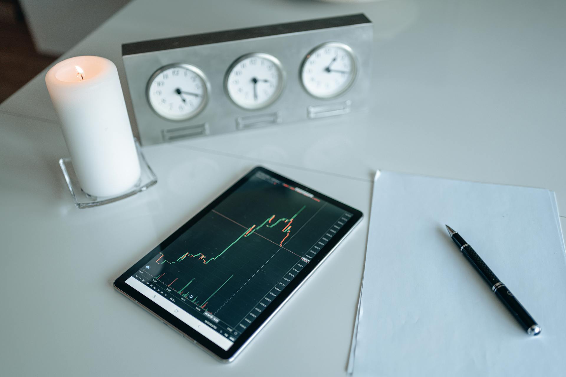 Tablet showing trading graph beside candle and papers in an office setting.