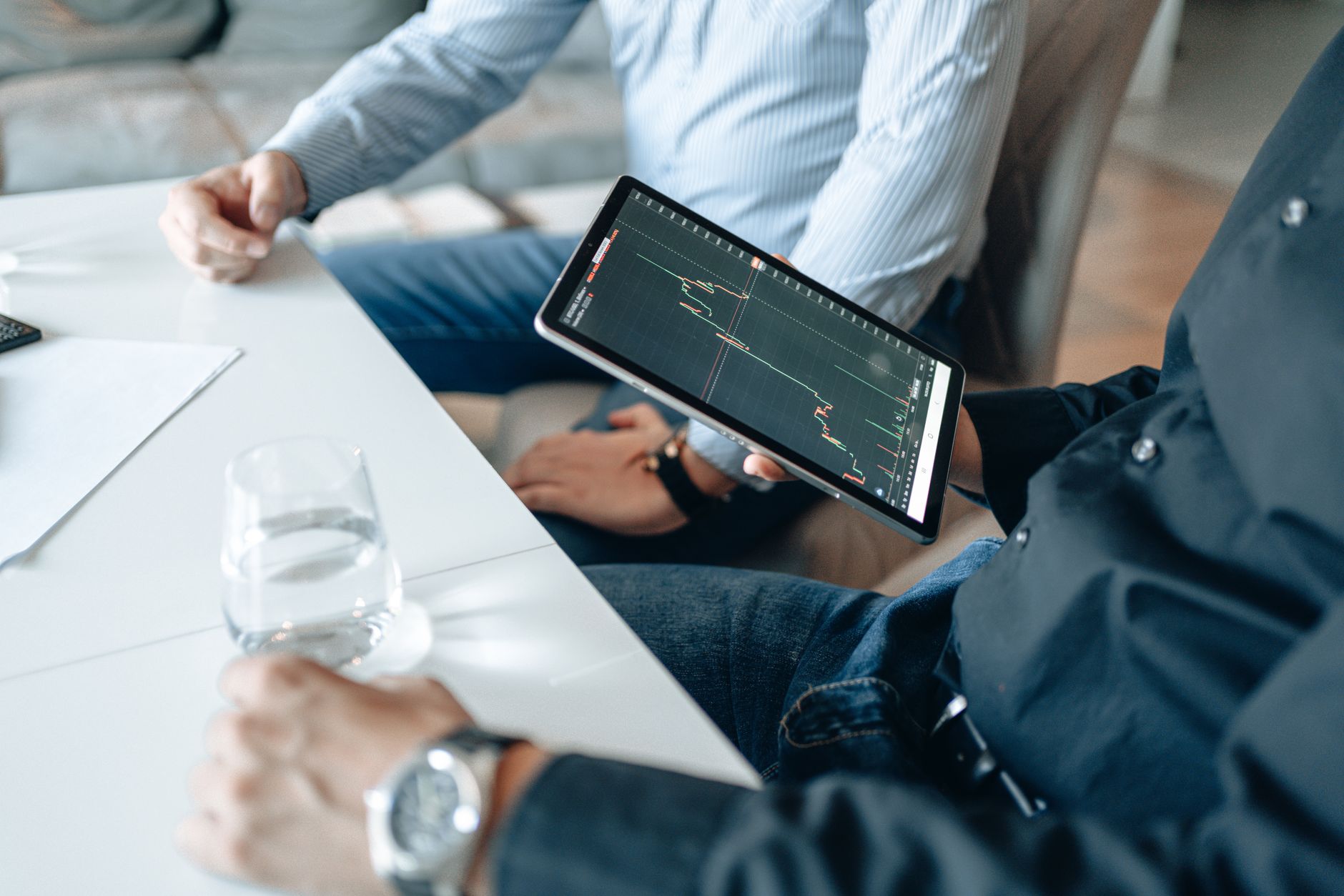 Two businessmen analyzing stock market data on a tablet in a modern office setting.