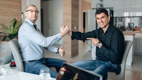 Free Two Men Sitting on Chairs Shaking Hands Stock Photo