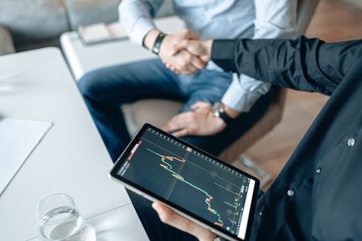 Two people shaking hands over a financial graph on a tablet, symbolizing a business agreement.