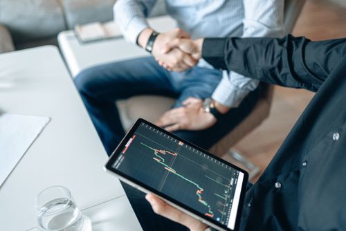 Free Two people shaking hands over a financial graph on a tablet, symbolizing a business agreement. Stock Photo