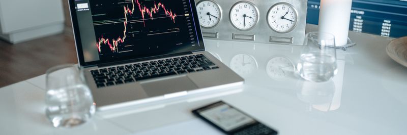A contemporary workspace featuring a laptop, candle, and clocks on a white desk, ideal for finance and technology themes.