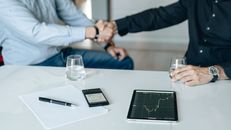 商务会议上，平板电脑上显示着握手和财务分析