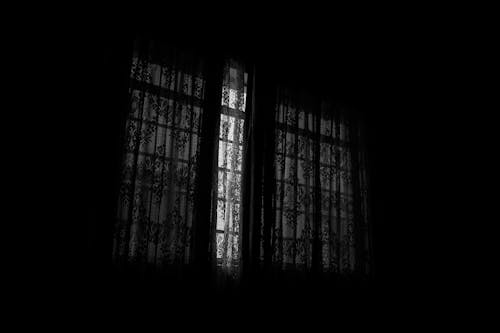 Black and white of dark room with closed drapes with creative ornaments and patterns hanging on window at home in darkness