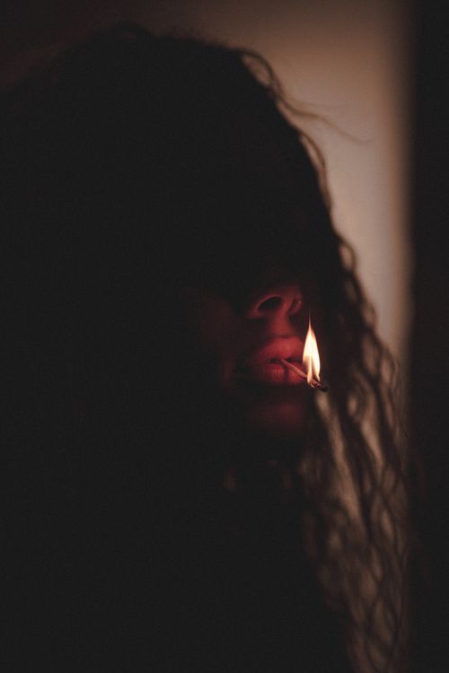 Free Anonymous female with long curly hair standing with hot burning match in mouth on blurred background in darkness in evening time Stock Photo
