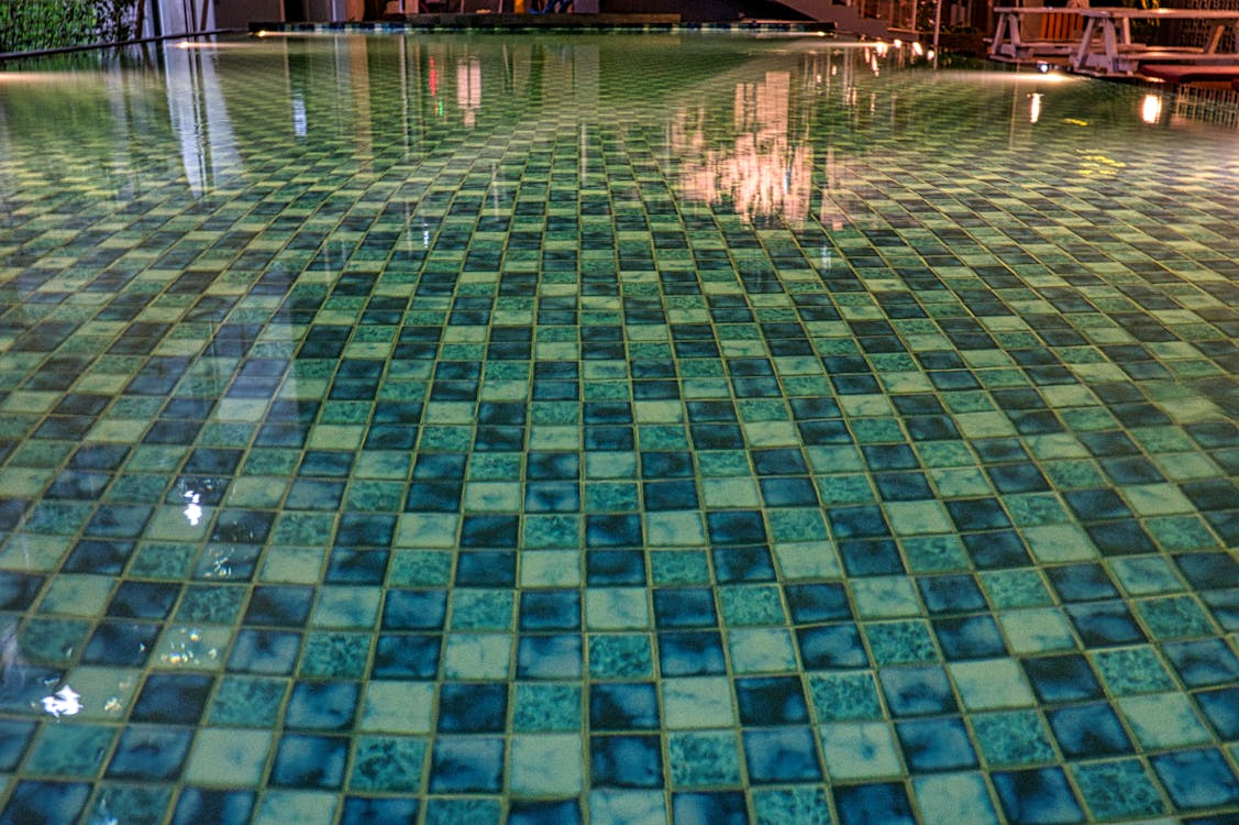 Swimming pool with blue tiles under constructions reflecting in shiny transparent aqua in daytime