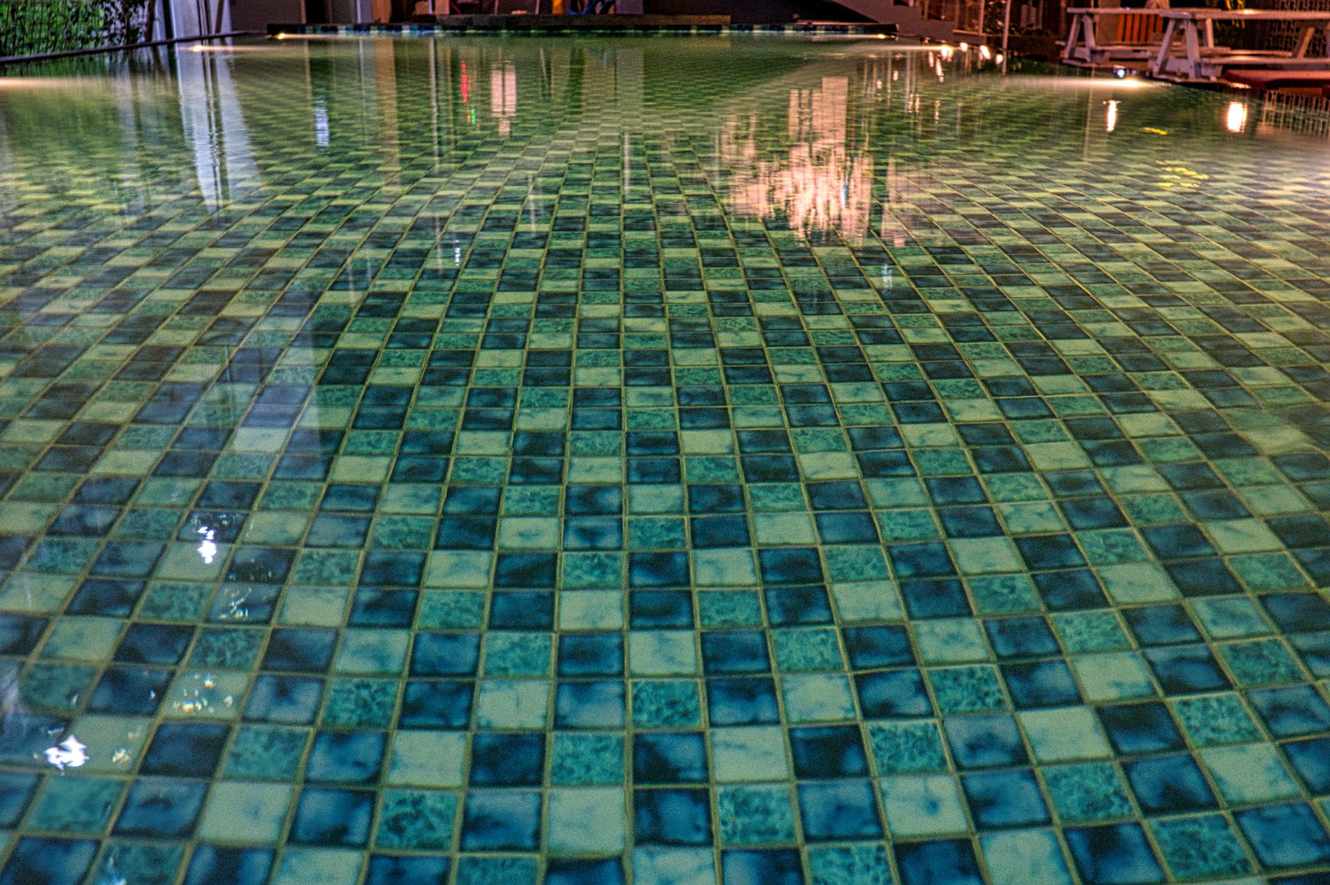 Swimming pool with blue tiles under constructions reflecting in shiny transparent aqua in daytime